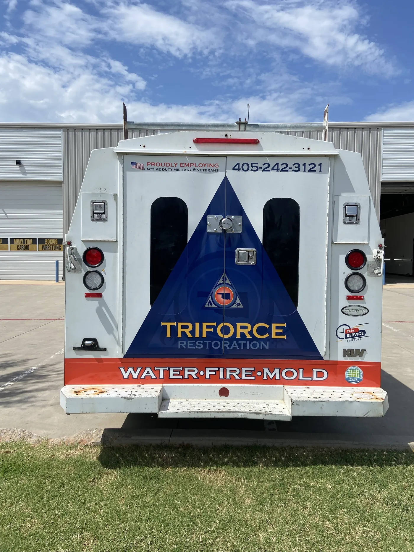 Rear doors of the Triforce Restoration service body with the blue triangle, logo, phone number, and Water Fire Mold band
